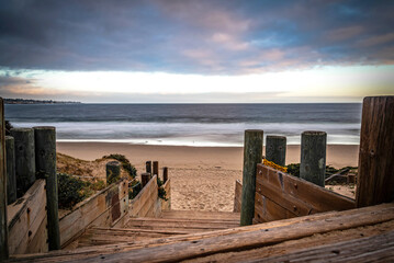 Wooden steps lead to a lead to a sunrise over the Pacific Ocean, soaking the beach in Monterey,...