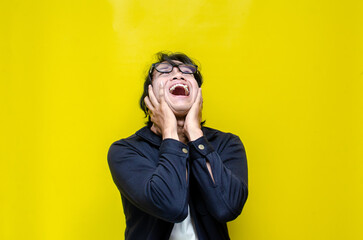 Hysterical mad depressed asian young man shouts and screams heavily opening mouth widely isolated over yellow background	