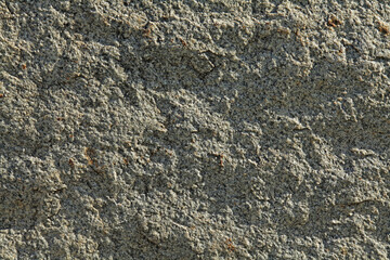 Grey uneven wall, texture, background. Relief rocky and shady surface of granite stone. Roug volcanic rock of light-grey color in urban development and decorative exterior. Granular igneous rock