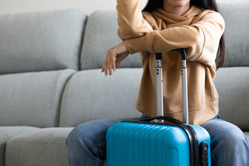 woman sitting on the sofa with her blue carry-on suitcase ready waiting to go on a trip