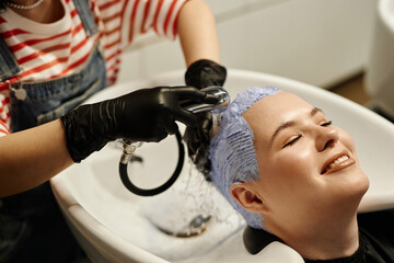 High angle closeup of smiling young woman enjoying hair wash in salon sink after bleaching