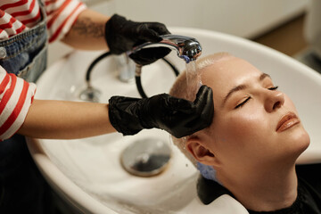 High angle closeup of young woman enjoying hair wash in beauty salon sink with hairstylist washing out bleach