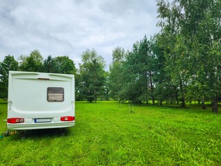 White retro styled camper van parked on lush green grass near the edge of a serene forest under a...