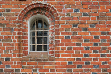 Wall of an ancient medieval building. There is a vaulted window, red brick with a pattern of black elements. Background. Texture.
