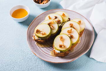 Pieces of pear, ricotta, honey and nuts on rye bruschettas on a plate on the table