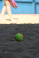 Close up of a beach tennis ball in the sand with a blurred woman in the background 