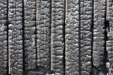 Black charred planks of the cladding of a burnt wooden house. Background. Texture.