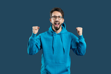 A man in a blue hoodie with his fists raised celebrating success, showing positive emotions...