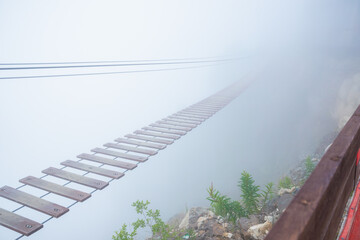 Tourist suspension bridge in deep fog. Hanging rope bridge vanishing