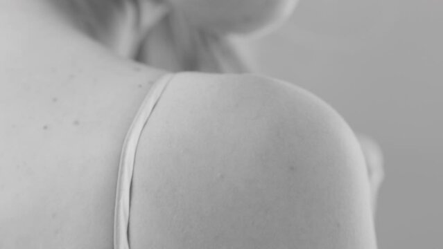 Woman looks over-shoulder and adjusts shirt strap close up