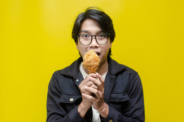 Funny expressive asian man holds fried chicken drumstick with satisfication face isolated over...