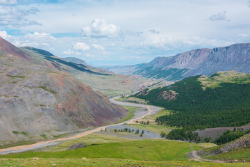 Sunny aerial top view to wide alpine valley with coniferous trees and long mountain river to...