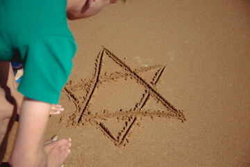 A young attractive student is relaxing by the seashore and drawing a star of David.