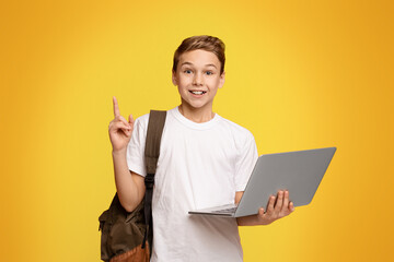 Cheerful boy holding laptop excited with idea or question, pointing finger up, number one, orange...