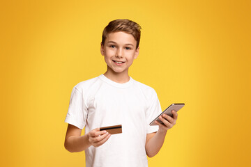 A young boy is seen holding a smart phone in one hand and a credit card in the other hand.