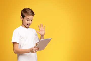 A young boy holding a laptop with one hand while making a hand gesture, possibly signaling...
