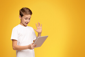 A young boy holding a laptop with one hand while making a hand gesture, possibly signaling excitement or sharing information.