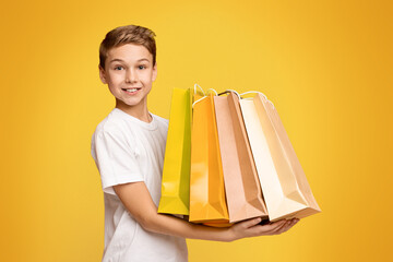Little shopper. Happy teen boy holding lots of colorful paper shopping bags in hands, orange studio...