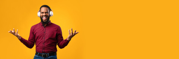 Fototapeta premium Online Music. Excited african american guy wearing white headset and dancing with joy isolated on yellow studio wall, copy space
