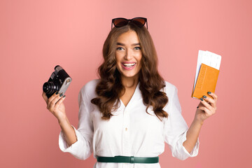A cheerful young woman with wavy hair is holding a classic black camera in one hand and an orange...