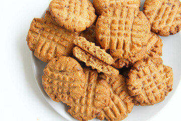 Stack of freshly baked peanut butter cookies on a light plate. The top cookie is broken in half to see the texture of cookies. White background.