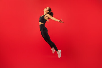 A woman in black sports bra and leggings is mid-air, jumping energetically. She is captured in a moment of athleticism and motion, showcasing her strength and agility.