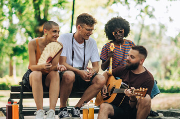 Group of interracial students playing guitar and singing in city park.