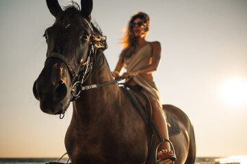 Obraz premium Selective focus on a horse head while a woman is riding it on a beach