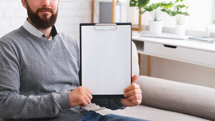 Confident psychotherapist showing white blank clipboard at camera, sitting in office, free space for announcement