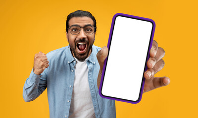 Indian man is holding up a cell phone in his hand, and his face displays a surprised expression. It...