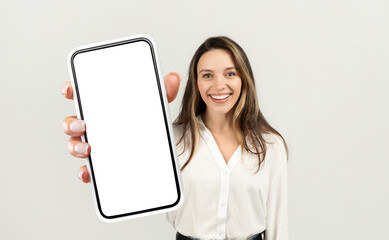 A woman entrepreneur holding a cell phone up in front of her with a blank screen visible. She...