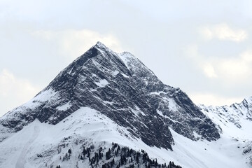 Berg in den Alpen mit Steinflanken Schnee und Eisfeldern und einer Lawine vor blauem Himmel mit leichter Bewölkung