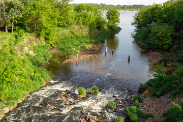 Several people are fishing in the not deep river.