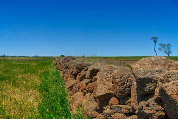 A stone wall made of volcanic rock separates a farm pasture and railroad tracks in the outback of Victoria, Australia.