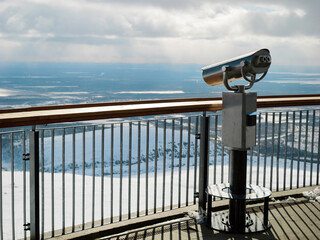 A coin-operated binocular on a viewing platform overlooks a snowy mountain range, offering...
