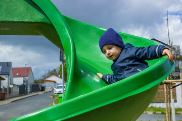 little boy 2-3 years slides down the green children's slide on the playground 