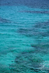 Türkisblaues Wasser am Mittelmeer mit Sand und Korallen und Gischt bei gutem Wetter Querformat