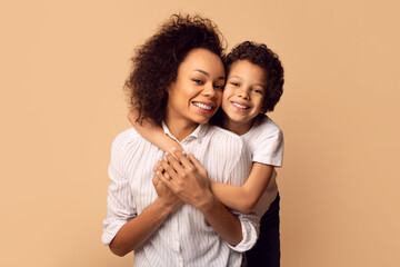 A joyful African American mother holds her son close in a tender hug, both wearing white shirts,...