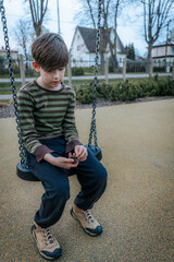 boy sits on the swing sad. A lonely child is waiting for a friend. A depressed and sad child