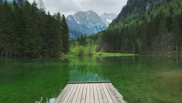 Alpine spring landscape with mountain lake and wooden footbridge. Plansarsko lake with green forest in Jezersko valley, Slovenia, Europe, 4k