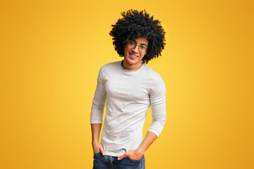 Self-confident black guy laughing with hands in pockets, orange studio background