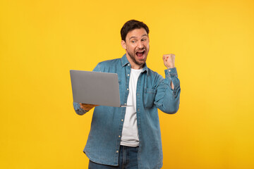 A man is joyfully celebrating while holding a laptop in his hands. He is likely reacting to good...