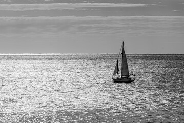 Black and white backlit image of a sailboat sailing in the Atlantic Ocean, with a beautiful sky as...