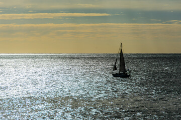Backlit image of a sailboat sailing in the Atlantic Ocean, with a beautiful sky as a background and...