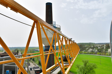 A yellow crane arm with a striking blue chimney against the sky