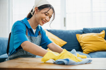 Smiling housewife in yellow gloves wipes table with care. Her routine involves cleaning home...