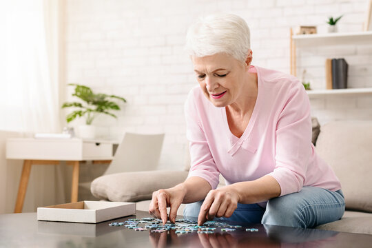 Activity can improve brain function. Elderly woman sitting at table and sorting jigsaw puzzle pieces, free space