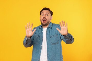 A young man with a beard stands against a bright yellow backdrop, showing a surprised expression...