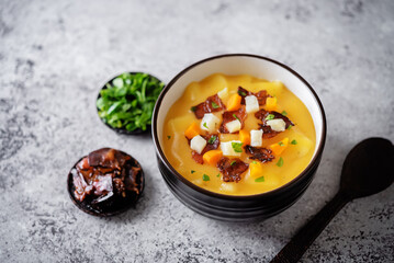 Potato carrot soup with fried bacon slices in a bowl