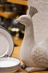 Ceramic peacock figurine in white, displayed prominently among plates. The peacock, with detailed...